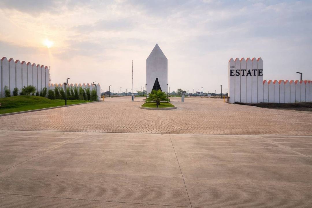 Landscaped estate entrance plaza with a white monument at sunset